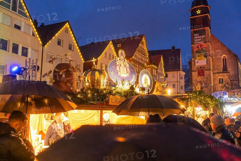 Crowd of people with umbrellas at an illuminated Christmas market in front of a church at night, Böblingen Christmas market, Germany
