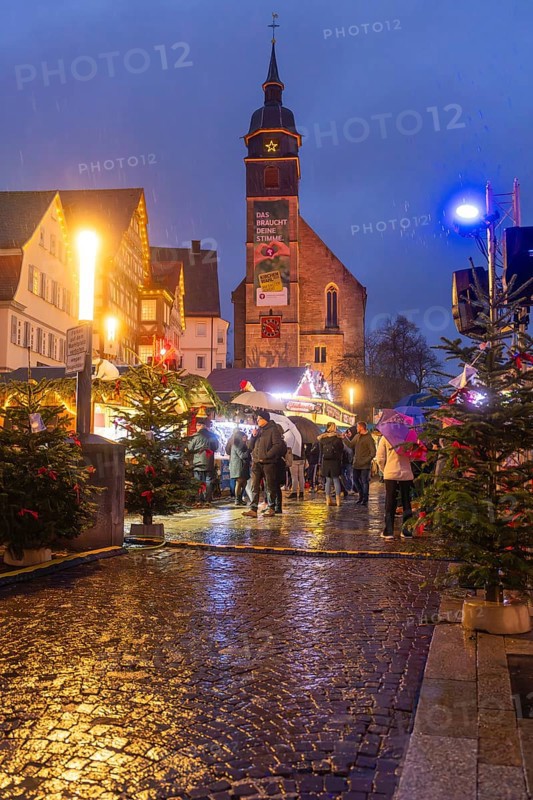 Christmas market with lights in front of a church, Christmas trees and people on wet cobblestones, Böblingen Christmas market, Germany
