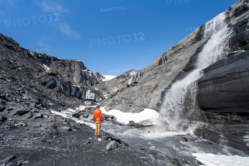 Tourist standing at a glacier stream, glacier ice and waterfall, Worthington Glacier State Recreational Site, Chugach Mountains, Alaska, USA