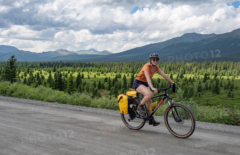 Young woman riding a bicycle on a dirt road through the tundra, mountainous landscape, Denali Park Road, Denali National Park and Preserve, Alaska, USA