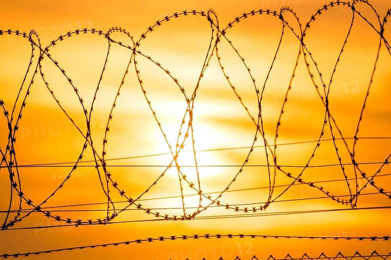 Sun sets behind barbed wire fence, bright orange and yellow tones, Baden-Württemberg, Germany