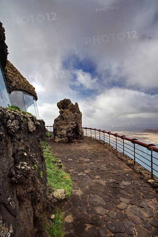 Rocky path with railing at Mirador del Rio viewpoint in cloudy sky, Haria Lanzarote, Canary Island