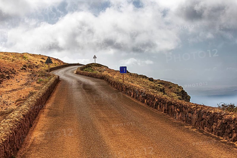 Secluded road along a rocky coast under a cloudy sky, Haria Lanzarote, Canary Island