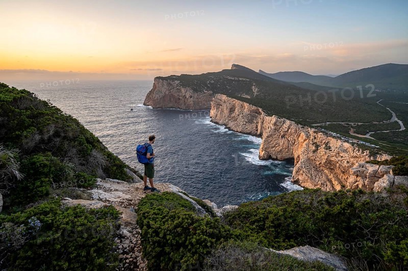 Tourist in front of coastal landscape at sunset, steep cliffs by the sea, cliffs in the evening light, Capo Caccia, Alghero, Sardinia