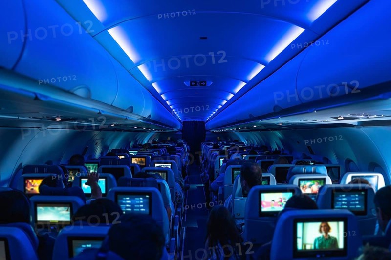 Passengers enjoying in flight entertainment while watching movies on personal screens, surrounded by a cozy atmosphere under blue ambient lighting in the aircraft cabin