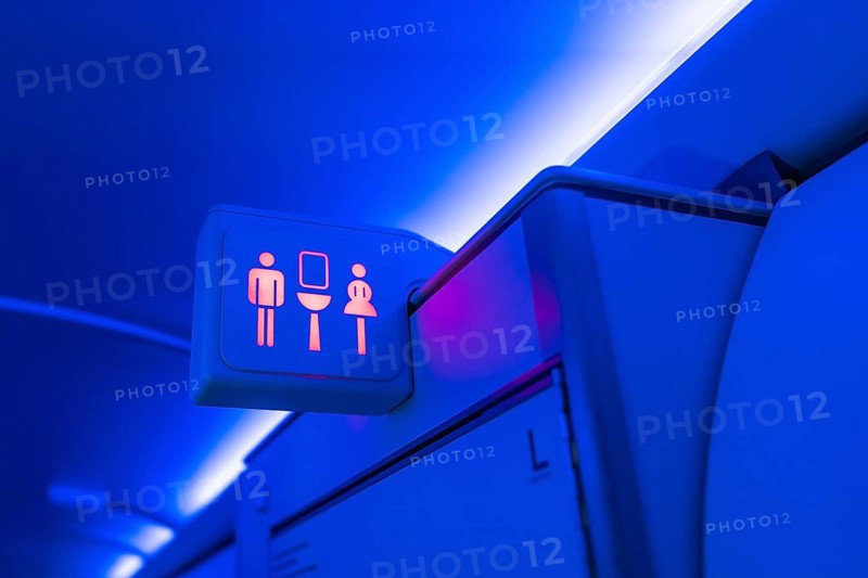 Illuminated restroom sign indicating availability with male and female symbols glowing red inside an airplane cabin with blue ambient lighting
