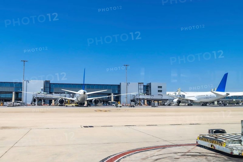 Two large passenger airplanes parked at airport gates under a bright sunny sky, waiting for passengers and preparing for their upcoming departures on a bustling day of travel