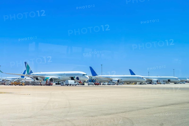 Several airplanes are parked on the tarmac at an airport, waiting for their next flights under a clear blue sky, with ground crew vehicles attending to them