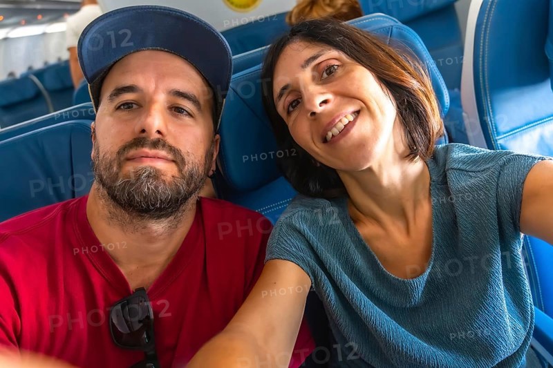 Happy couple taking a selfie on an airplane, enjoying their flight while capturing joyful moments together. Smiling and sharing their adventure high above the ground