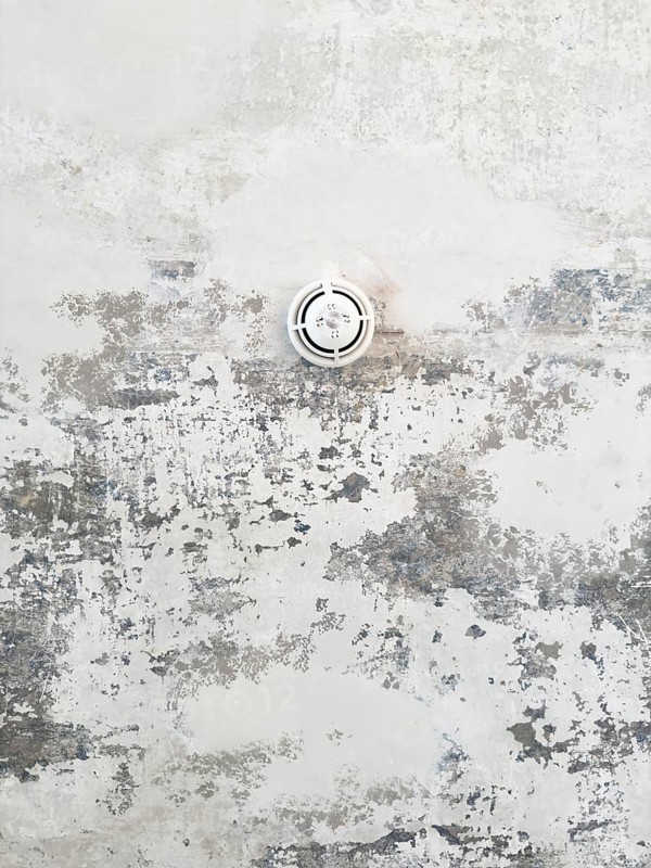 Round ceiling sprinkler nozzle in minimalistic concrete ceiling with chipped paint and abstract structure, Wuppertal, Germany
