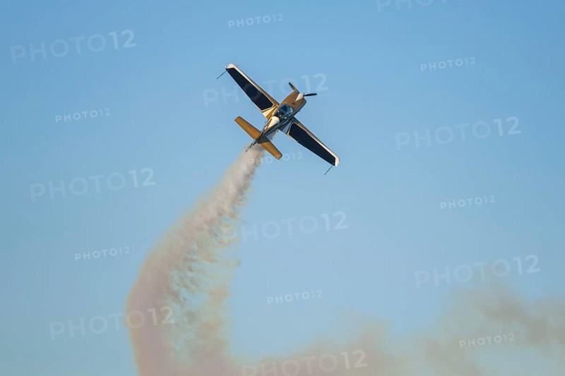 Golden stunt aerobatic plane performing stunts in blue sky with smoke trail. Concept of speed, difficulty, precision, risk