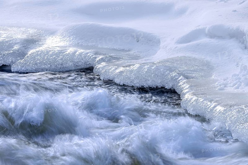 Ice formation formed by frost and freezing cold temperatures over running water of stream along riverbank / river bank in winter