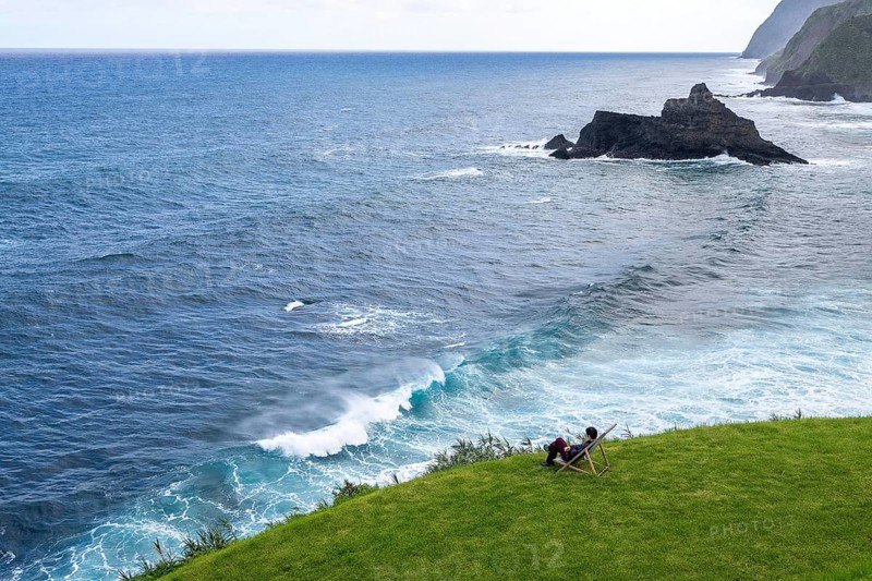 Woman sitting comfortably in deckchair in a meadow and watching waves in the sea, Madeira, Portugal
