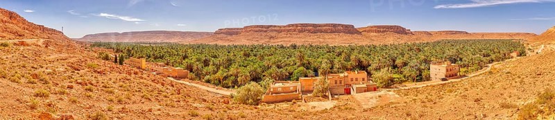 A wide panorama with an oasis, many palm trees and buildings against a mountain backdrop, Ziz Canyon in Morocco