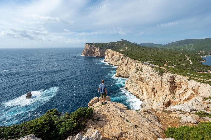 Tourist enjoying the view of steep cliffs by the sea, coastal landscape, cliffs on the Capo Caccia headland, Alghero, Sardinia, Italy