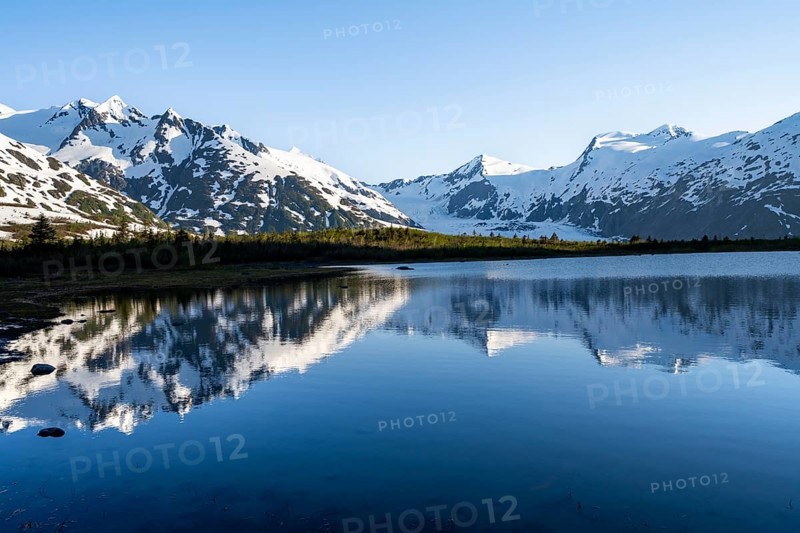 Mountain peaks with Portage Glacier glacier and snow reflected in Divide Lake mountain lake in evening light, Portage Pass Trail, Whittier, Alaska, USA