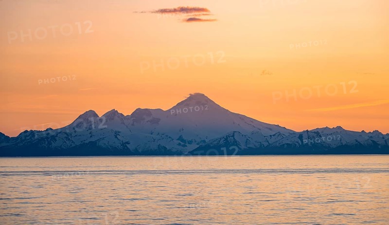 View of Cook Inlet on white mountain peaks of Mount Iliamna at sunset, picturesque golden light of the midnight sun, mountains of the Aleutian Range, Anchor Point, Anchor River State Recreation Area, Alaska, USA