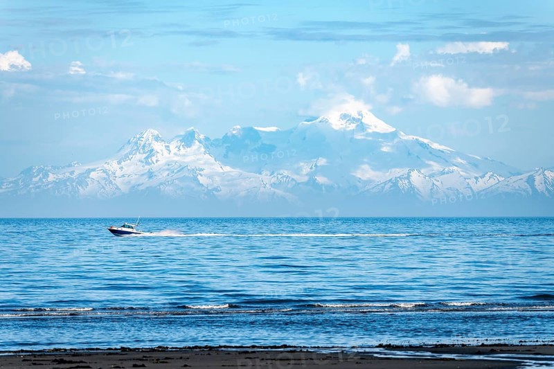 View over Cook Inlet to white mountain peaks of Mount Iliamna, motor boat rides on the ocean, mountains of the Aleutian Range, Anchor Point, Anchor River State Recreation Area, Alaska, USA