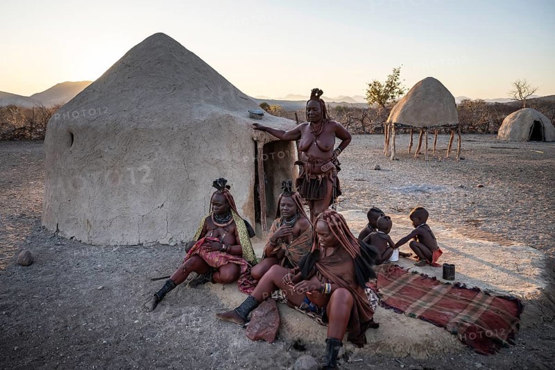 Married Himba woman with their babies in their arms sitting in front of the first woman's hut, in the morning, traditional Himba village, Kaokoveld, Kunene, Namibia