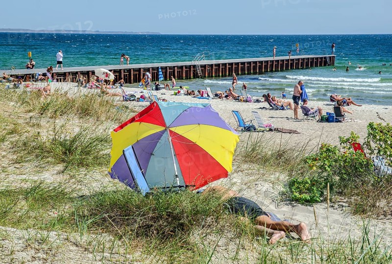 Colorful parasol on the beach with jetty and sunbathing people in Ystad, Skåne County, Sweden, Scandinavia