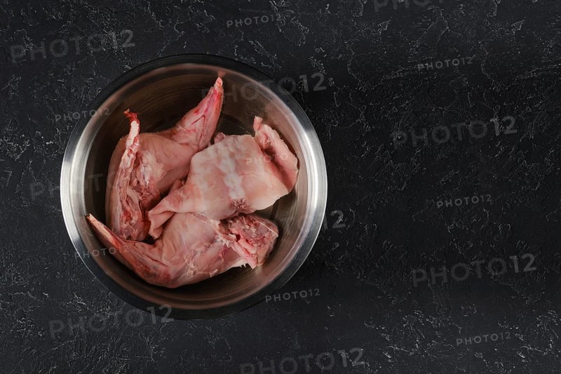 Fresh rabbit hind legs and a saddle are soaked in water with vinegar in a metal bowl. The process of softening raw meat and reducing the taste of wild rabbit