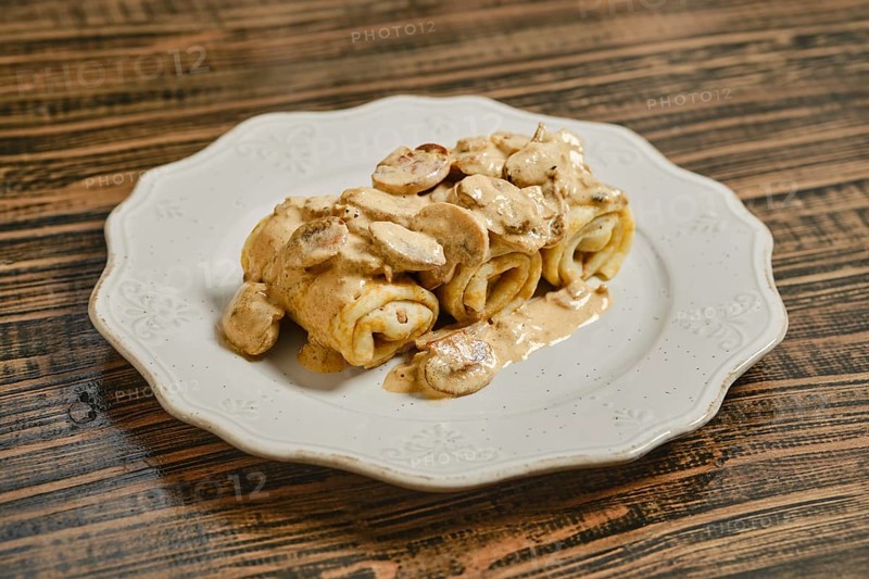 Tasty crepes filled with savory meat and topped with a creamy mushroom sauce, served on a decorative white plate