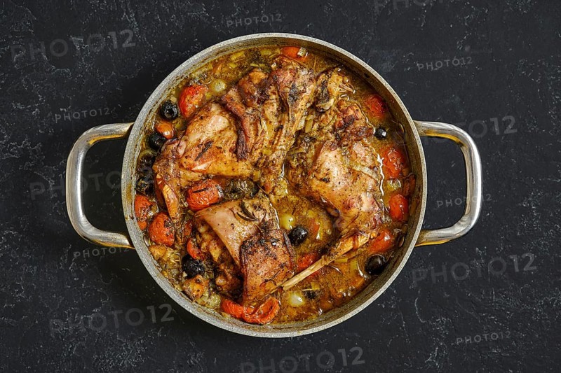 A delicious rabbit hind leg stew simmers in a large pot, featuring juicy meat surrounded by carrots, olives, and other vegetables in a rich sauce. Ideal for a cozy dinner or family meal