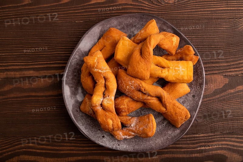 Crunchy biscuit Brushwood cookies sprinkled with powdered sugar on brown wooden background, top view, flat lay, close up