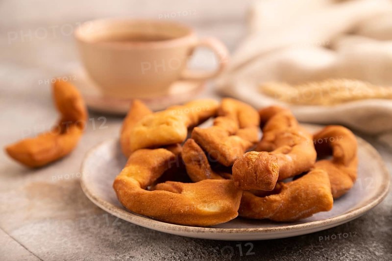 Crunchy biscuit Brushwood cookies sprinkled with powdered sugar on brown concrete background and linen textile, cup of coffee, side view, selective focus