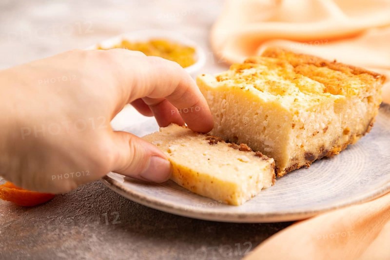 ?ottage cheese ?asserole, Curd cake, with dried apricots and raisins with hand on brown concrete background and orange textile, side view, selective focus, minimalism