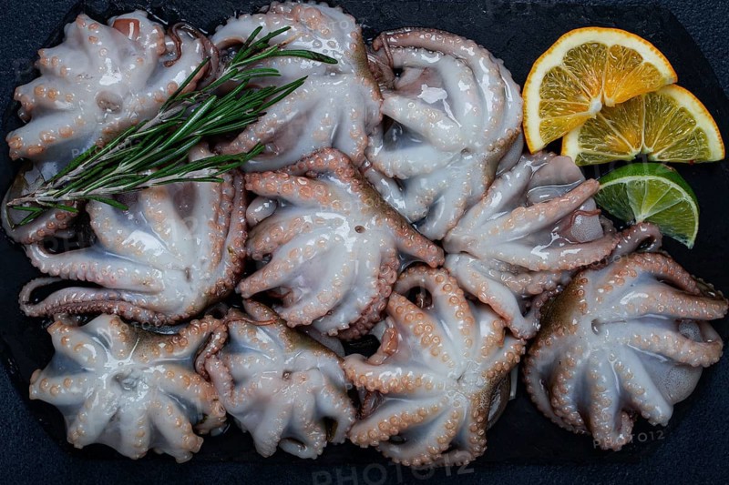 Fresh baby octopus, on black slate, with lemon and greenery, top view, no people