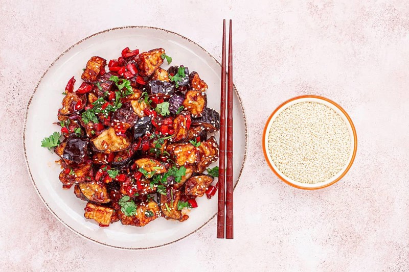Fried eggplant, Chinese style, in sweet and sour sauce, with pepper and sesame seeds. on a white plate