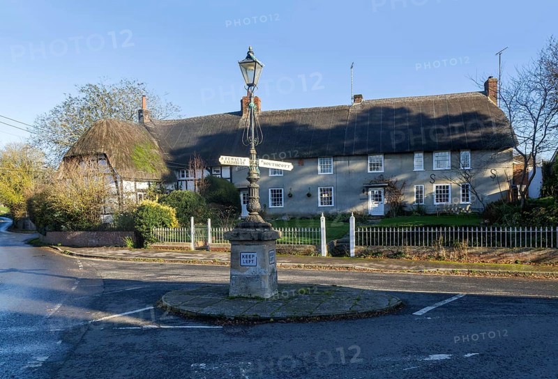 Historic signpost with direction arrows, thatched cottages in village of Pewsey, Wiltshire, England, UK