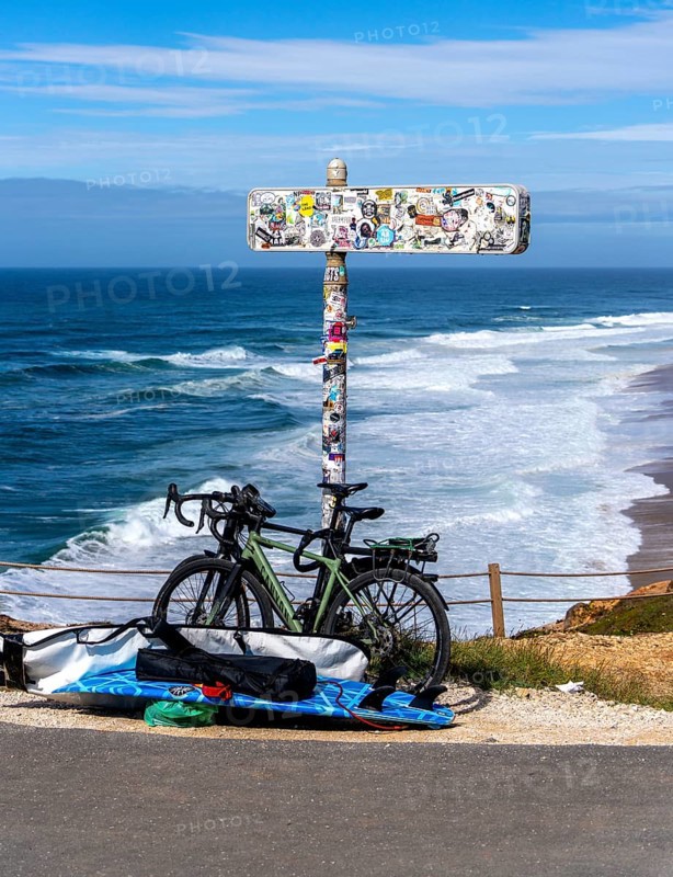 Sticker-covered sign with bicycles and surfboards, Nazaré, Portugal