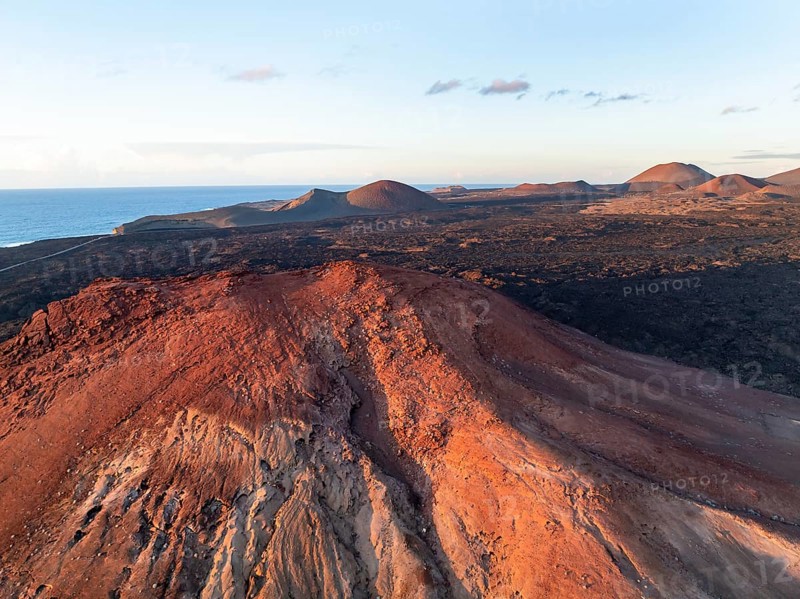 Picturesque volcanic landscape in evening light, red volcano Montaña Bermeja between lava fields, aerial view, Lanzarote, Canary Islands, Spain