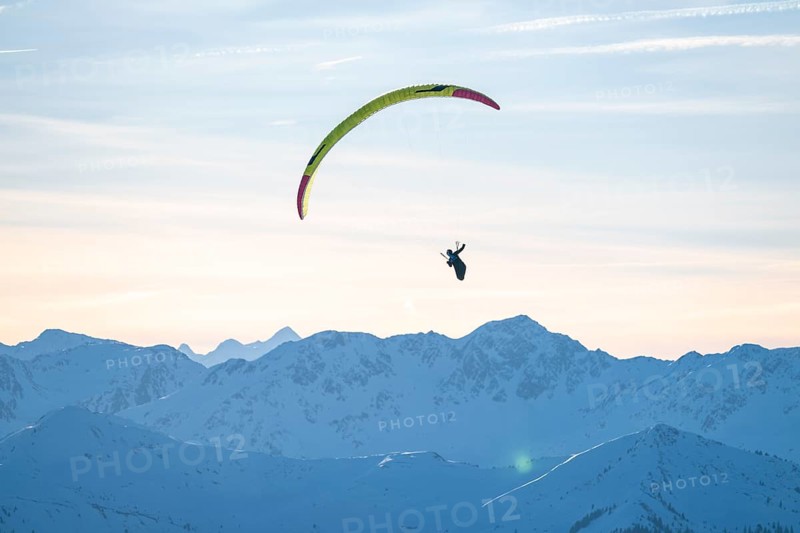 Paragliders flying over snowy mountain peaks in winter in evening light, Kitzbühel Alps, Tyrol, Austria