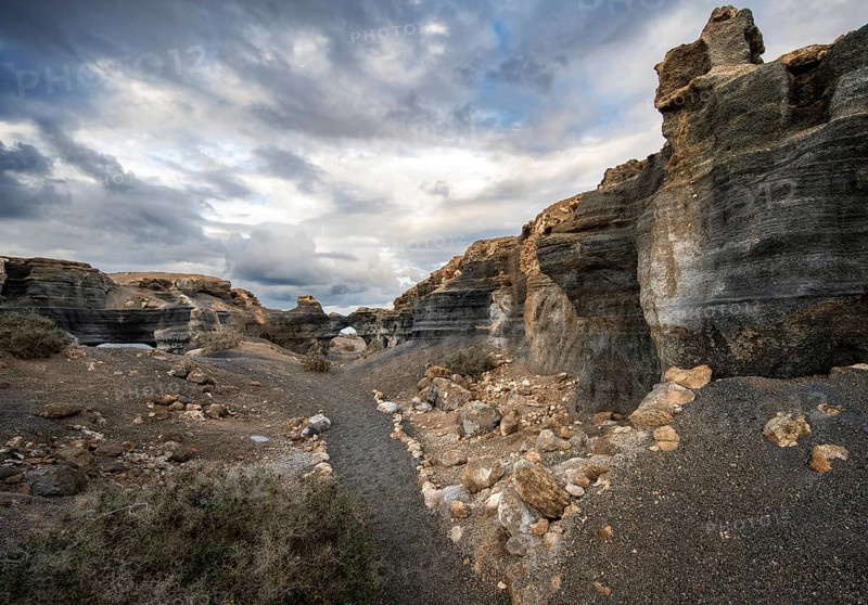 Eroded rock formations, volcanic landscape with dramatic cloudy skies, Ciudad Estratificada or Los Roferos, Antigua Rofera de Teseguite, Lanzarote, Canary Islands, Spain