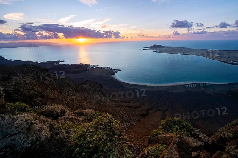 View from steep cliffs to sea and coast with sun stars, Mirador del Porrito viewpoint at sunset, Lanzarote, Canary Islands, Spain