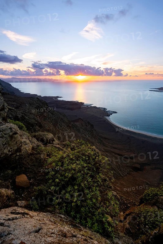 View from steep cliffs to sea and coast with sun stars, Mirador del Porrito viewpoint at sunset, Lanzarote, Canary Islands, Spain