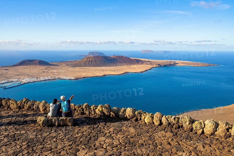 Tourists on a bench on the viewing platform at the Mirador del Río viewpoint, in the evening light, view of the sea and of the island of La Graciosa with volcanic craters, designed by artist César Manrique, Lanzarote, Canary Islands, Spain