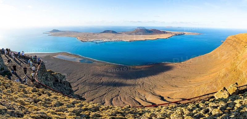 View of La Graciosa island with volcanic craters in the evening light, tourists on an observation deck at the Mirador del Río viewpoint designed by artist César Manrique, Lanzarote, Canary Islands, Spain
