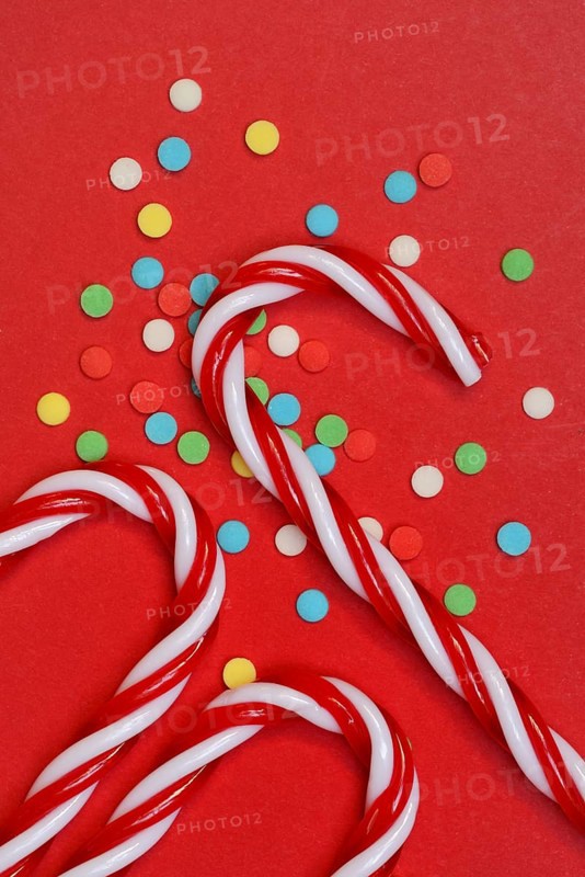 Candy canes and sugar confetti against red background, Christmas