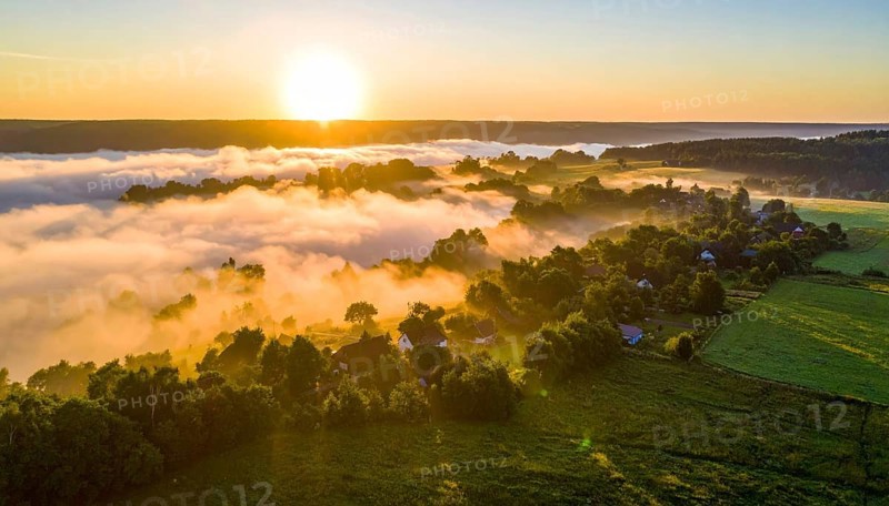 Sunrise over a fog covered village in a rural landscape, golden morning light, serene autumn atmosphere, hills and mountains in the background, AI generated