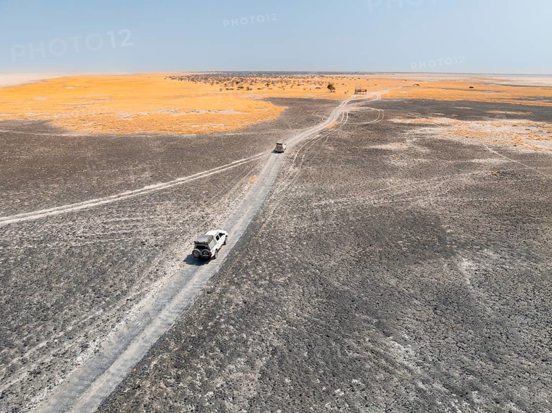 Aerial view, two off-road cars driving on a salt pan, arid landscape, Botswana