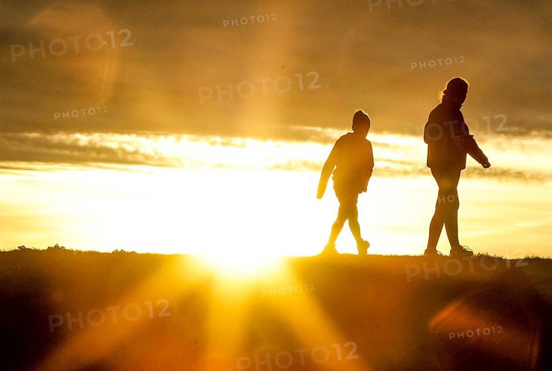 Woman and child walk across a dike on the island of Fehmarn at sunset, 13.10.2025, Fehmarn, Schleswig-Holstein, Germany