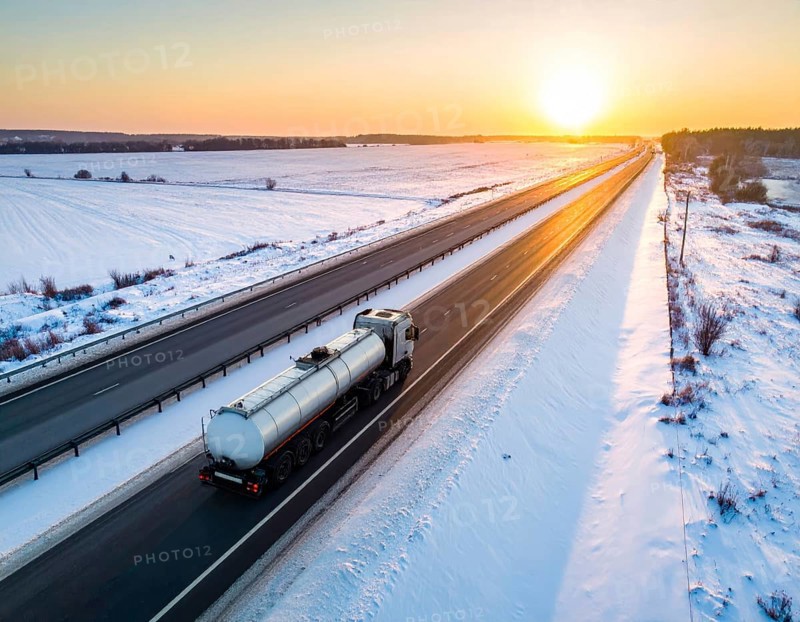 Petrol cargo truck lorry tanker driving on highway hauling oil products at sunrise, wide snowy landscape in winter, AI generated