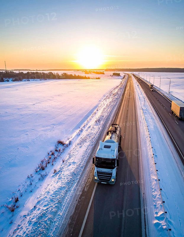 Petrol cargo truck lorry tanker driving on highway hauling oil products at sunrise, wide snowy landscape in winter, AI generated