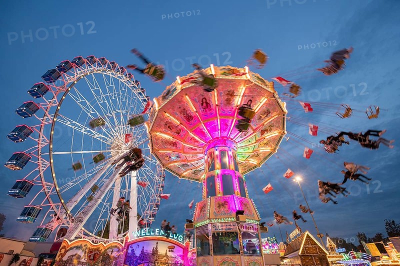 An illuminated chain carousel and Ferris wheel at night at a funfair, people swinging on chains, Bad Cannstatt, Stuttgart, Baden-Württemberg, Germany