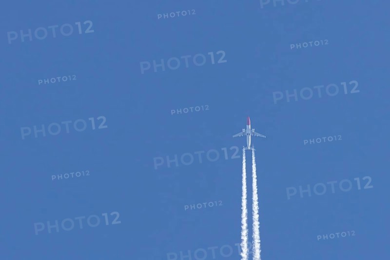 Boeing 737 jet passenger aircraft of Norweign Air with a vapour trial or contrail behind flying in a blue sky, England, United Kingdom