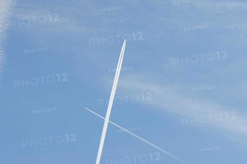 Two jet passenger aircraft with vapour trails or contrails flying in a blue sky crossing making a cross, England, United Kingdom